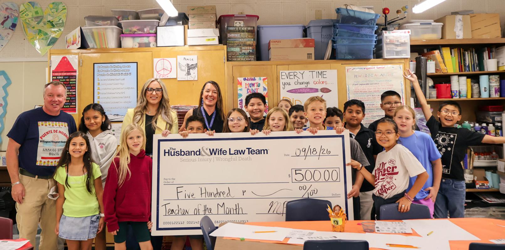 Students and staff gather to celebrate a special Teacher of the Month recognition as a $500 award from the Husband & Wife Law Team is presented in honor of an educator's dedication and positive impact in the classroom.