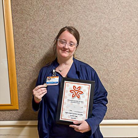Nurse Elizabeth holds her Guardian Angel award and pin while smiling