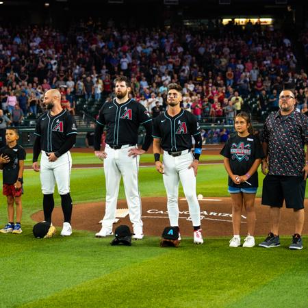 Three Diamondbacks players with two Kids Take The Field winners and their father figures during the national anthem