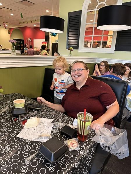 A smiling adult and child sit together at a table with food, coloring pages, and drinks inside Chicken Salad Chick, an Albuquerque neighborhood restaurant.