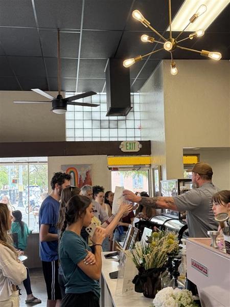 Happy, hungry customers line up at the counter as a barista hands a drink to a smiling woman.