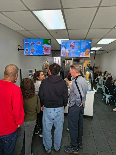 Customers wait in line at Crepes and Waffles beneath bright menu screens