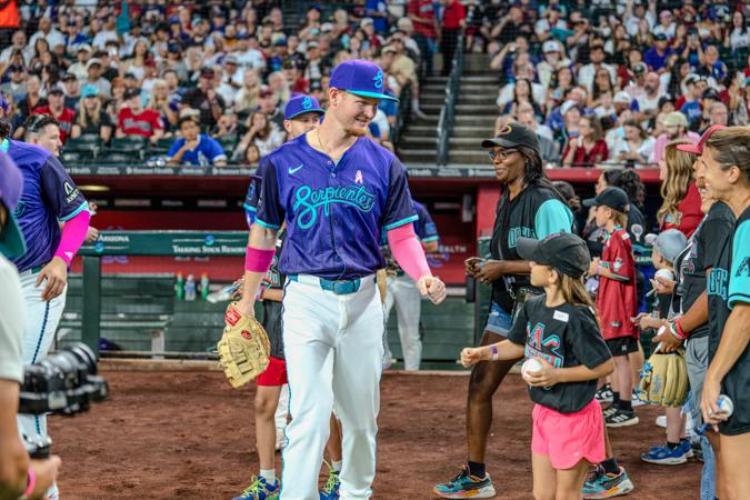 Baseball player in blue uniform interacts with young fans on the field, surrounded by a crowd in a stadium.