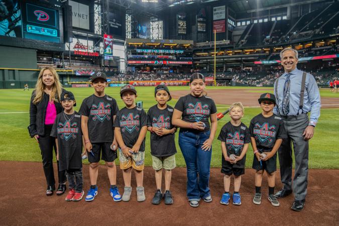 A group of excited kids at Chase Field during the Arizona Diamondbacks Kids Take the Field event. Posing for a photo with Alexis & Mark Breyer from the Husband & Wife Law Team.