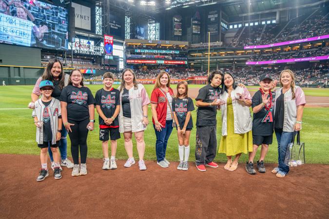 On the big‑league stage. The Kids Take the Field winners pose together on the stadium field, grinning wide during this special event moment.