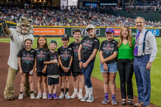 A group of excited kids at Chase Field during the Arizona Diamondbacks Kids Take the Field event. Posing for a photo with Alexis & Mark Breyer from the Husband & Wife Law Team.