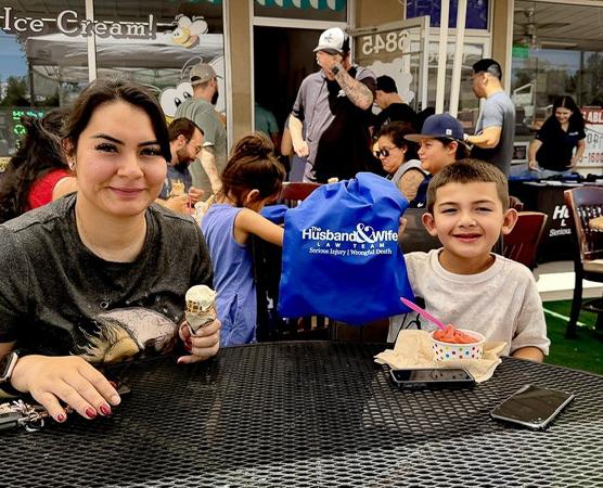 A mother and child enjoy frozen custard together at Busy Bee Frozen Custard, with the child proudly carrying a Husband & Wife Law Team drawstring bag during a fun community event.