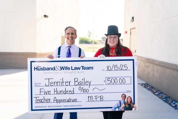 Two people smiling, holding a large check for $500 made out to Jennifer Bailey from The Husband & Wife Law Team.